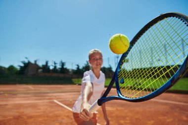 Güneşli bir günde tenis kortunun modern estetiğiyle çevrili profesyonel tenis yeteneklerini sergileyen genç bir kızın yakın plan fotoğrafı.