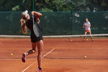 Genç kızlar güneşli bir günde canlı bir tenis maçında modern bir tenis kortunda yeteneklerini ve heveslerini gösteriyorlar.