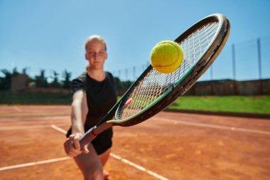 Güneşli bir günde tenis kortunun modern estetiğiyle çevrili profesyonel tenis yeteneklerini sergileyen genç bir kızın yakın plan fotoğrafı.