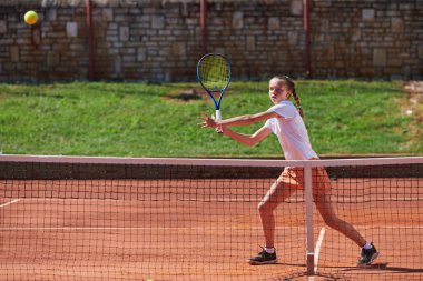 Güneşli bir günde tenis kortunun modern estetiğiyle çevrili profesyonel tenis yetenekleri sergileyen genç bir kız.