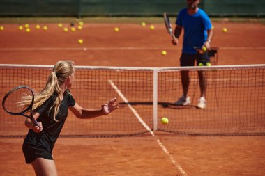 Profesyonel bir tenisçi ve onun koçu tenis kortunda güneşli bir günde antrenman yapıyorlar. Profesyonel bir tenisçinin antrenmanı ve hazırlığı.