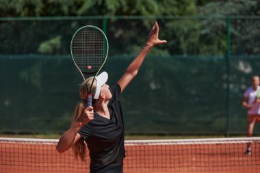 Genç kızlar güneşli bir günde canlı bir tenis maçında modern bir tenis kortunda yeteneklerini ve heveslerini gösteriyorlar.