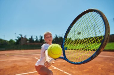 Güneşli bir günde tenis kortunun modern estetiğiyle çevrili profesyonel tenis yeteneklerini sergileyen genç bir kızın yakın plan fotoğrafı.