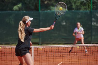 Genç kızlar güneşli bir günde canlı bir tenis maçında modern bir tenis kortunda yeteneklerini ve heveslerini gösteriyorlar.