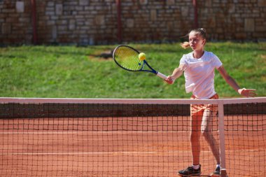 Güneşli bir günde tenis kortunun modern estetiğiyle çevrili profesyonel tenis yetenekleri sergileyen genç bir kız.