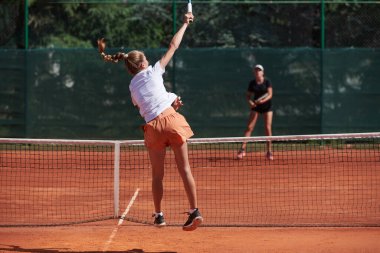 Genç kızlar güneşli bir günde canlı bir tenis maçında modern bir tenis kortunda yeteneklerini ve heveslerini gösteriyorlar.