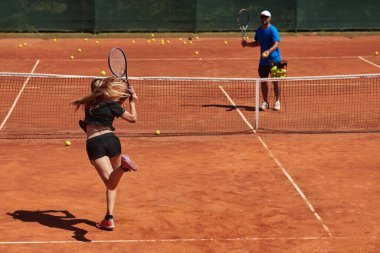 Profesyonel bir tenisçi ve onun koçu tenis kortunda güneşli bir günde antrenman yapıyorlar. Profesyonel bir tenisçinin antrenmanı ve hazırlığı.