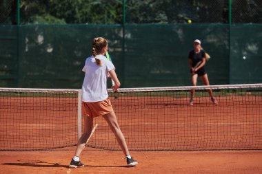 Genç kızlar güneşli bir günde canlı bir tenis maçında modern bir tenis kortunda yeteneklerini ve heveslerini gösteriyorlar.