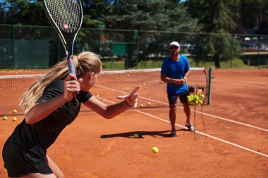 Profesyonel bir tenisçi ve onun koçu tenis kortunda güneşli bir günde antrenman yapıyorlar. Profesyonel bir tenisçinin antrenmanı ve hazırlığı.