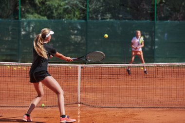 Genç kızlar güneşli bir günde canlı bir tenis maçında modern bir tenis kortunda yeteneklerini ve heveslerini gösteriyorlar.