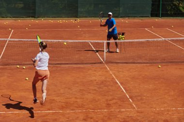 Profesyonel bir tenisçi ve onun koçu tenis kortunda güneşli bir günde antrenman yapıyorlar. Profesyonel bir tenisçinin antrenmanı ve hazırlığı.