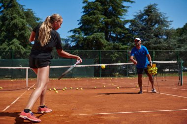 Profesyonel bir tenisçi ve onun koçu tenis kortunda güneşli bir günde antrenman yapıyorlar. Profesyonel bir tenisçinin antrenmanı ve hazırlığı.