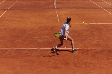Güneşli bir günde tenis kortunun modern estetiğiyle çevrili profesyonel tenis yetenekleri sergileyen genç bir kız.