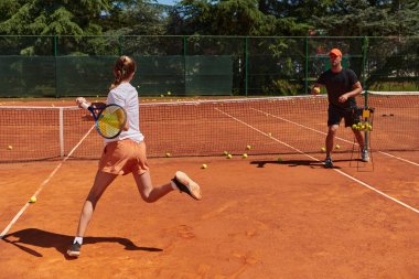 Profesyonel bir tenisçi ve onun koçu tenis kortunda güneşli bir günde antrenman yapıyorlar. Profesyonel bir tenisçinin antrenmanı ve hazırlığı.