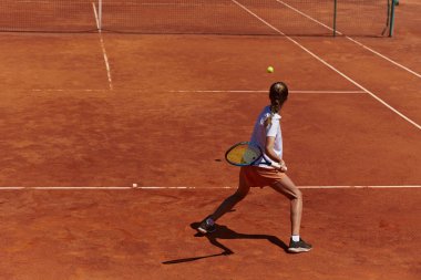 Güneşli bir günde tenis kortunun modern estetiğiyle çevrili profesyonel tenis yetenekleri sergileyen genç bir kız.