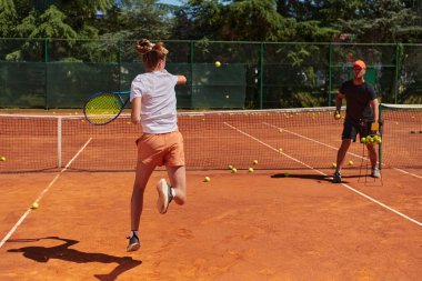 Profesyonel bir tenisçi ve onun koçu tenis kortunda güneşli bir günde antrenman yapıyorlar. Profesyonel bir tenisçinin antrenmanı ve hazırlığı.