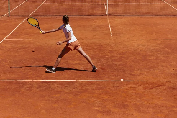 在阳光灿烂的日子里 一个年轻姑娘在一场比赛中表现出了专业的网球技巧 四周环绕着现代网球场的美感 — 图库照片