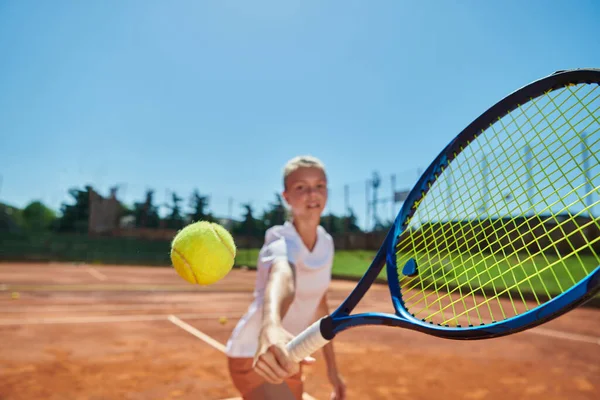 Close up photo of a young girl showing professional tennis skills in a competitive match on a sunny day, surrounded by the modern aesthetics of a tennis court