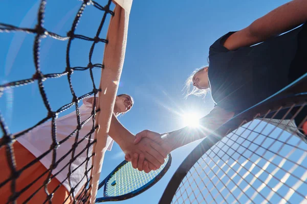 在一个阳光灿烂的日子里 两名女网球选手微笑着握手 在一场比赛之后 展现了运动员的风范和友谊 — 图库照片