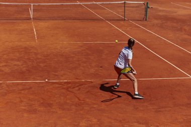 Güneşli bir günde tenis kortunun modern estetiğiyle çevrili profesyonel tenis yetenekleri sergileyen genç bir kız.