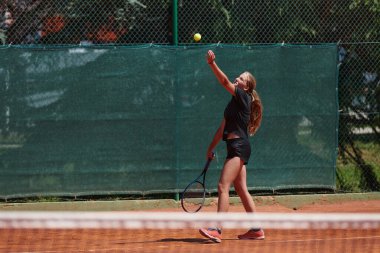 Güneşli bir günde tenis kortunun modern estetiğiyle çevrili profesyonel tenis yetenekleri sergileyen genç bir kız.