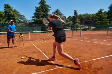 Profesyonel bir tenisçi ve onun koçu tenis kortunda güneşli bir günde antrenman yapıyorlar. Profesyonel bir tenisçinin antrenmanı ve hazırlığı.
