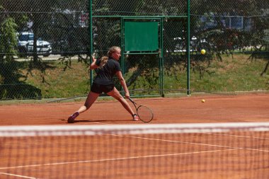 Güneşli bir günde tenis kortunun modern estetiğiyle çevrili profesyonel tenis yetenekleri sergileyen genç bir kız.