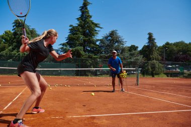 Profesyonel bir tenisçi ve onun koçu tenis kortunda güneşli bir günde antrenman yapıyorlar. Profesyonel bir tenisçinin antrenmanı ve hazırlığı.