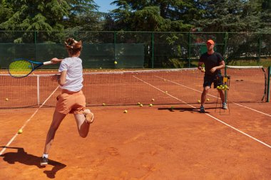Profesyonel bir tenisçi ve onun koçu tenis kortunda güneşli bir günde antrenman yapıyorlar. Profesyonel bir tenisçinin antrenmanı ve hazırlığı.
