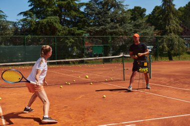 Profesyonel bir tenisçi ve onun koçu tenis kortunda güneşli bir günde antrenman yapıyorlar. Profesyonel bir tenisçinin antrenmanı ve hazırlığı.