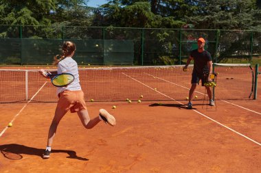Profesyonel bir tenisçi ve onun koçu tenis kortunda güneşli bir günde antrenman yapıyorlar. Profesyonel bir tenisçinin antrenmanı ve hazırlığı.