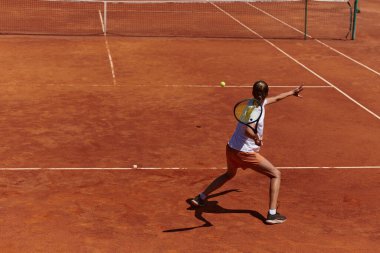 Güneşli bir günde tenis kortunun modern estetiğiyle çevrili profesyonel tenis yetenekleri sergileyen genç bir kız.