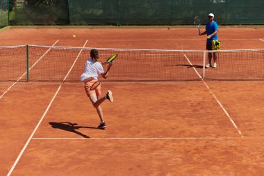 Profesyonel bir tenisçi ve onun koçu tenis kortunda güneşli bir günde antrenman yapıyorlar. Profesyonel bir tenisçinin antrenmanı ve hazırlığı.