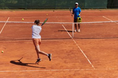 Profesyonel bir tenisçi ve onun koçu tenis kortunda güneşli bir günde antrenman yapıyorlar. Profesyonel bir tenisçinin antrenmanı ve hazırlığı.