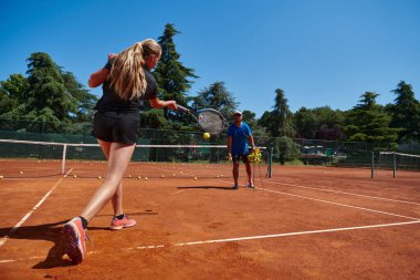 Profesyonel bir tenisçi ve onun koçu tenis kortunda güneşli bir günde antrenman yapıyorlar. Profesyonel bir tenisçinin antrenmanı ve hazırlığı.