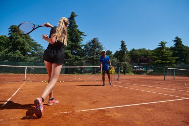 Profesyonel bir tenisçi ve onun koçu tenis kortunda güneşli bir günde antrenman yapıyorlar. Profesyonel bir tenisçinin antrenmanı ve hazırlığı.