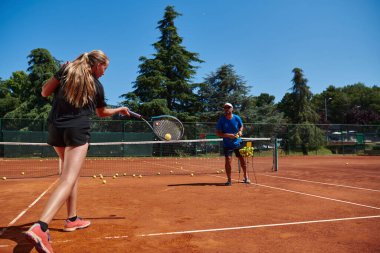Profesyonel bir tenisçi ve onun koçu tenis kortunda güneşli bir günde antrenman yapıyorlar. Profesyonel bir tenisçinin antrenmanı ve hazırlığı.