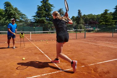 Profesyonel bir tenisçi ve onun koçu tenis kortunda güneşli bir günde antrenman yapıyorlar. Profesyonel bir tenisçinin antrenmanı ve hazırlığı.