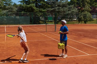 Profesyonel bir tenisçi ve onun koçu tenis kortunda güneşli bir günde antrenman yapıyorlar. Profesyonel bir tenisçinin antrenmanı ve hazırlığı.