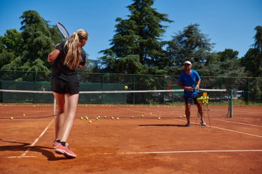 Profesyonel bir tenisçi ve onun koçu tenis kortunda güneşli bir günde antrenman yapıyorlar. Profesyonel bir tenisçinin antrenmanı ve hazırlığı.