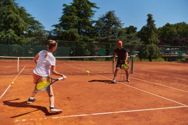 Profesyonel bir tenisçi ve onun koçu tenis kortunda güneşli bir günde antrenman yapıyorlar. Profesyonel bir tenisçinin antrenmanı ve hazırlığı.