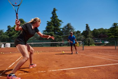Profesyonel bir tenisçi ve onun koçu tenis kortunda güneşli bir günde antrenman yapıyorlar. Profesyonel bir tenisçinin antrenmanı ve hazırlığı.
