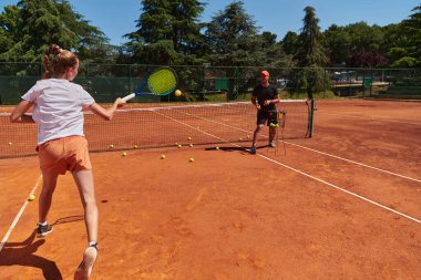 Profesyonel bir tenisçi ve onun koçu tenis kortunda güneşli bir günde antrenman yapıyorlar. Profesyonel bir tenisçinin antrenmanı ve hazırlığı.