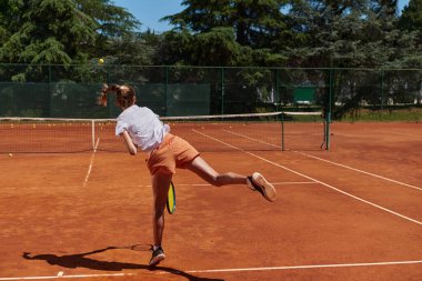 Tenis oyuncusu dikkatle odaklanarak, tenis kortuna yaptığı servisi hassasiyetle ve kararlılıkla mükemmelleştiriyor ve yeteneklerini geliştirmeye olan bağlılığını gösteriyor.