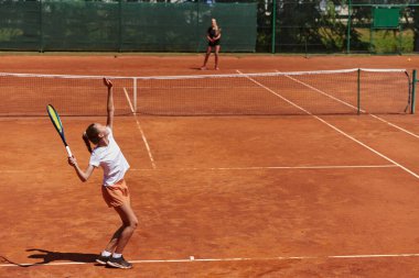 Genç kızlar güneşli bir günde canlı bir tenis maçında modern bir tenis kortunda yeteneklerini ve heveslerini gösteriyorlar.
