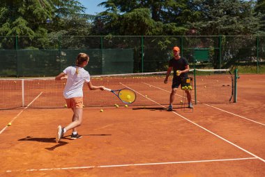 Profesyonel bir tenisçi ve onun koçu tenis kortunda güneşli bir günde antrenman yapıyorlar. Profesyonel bir tenisçinin antrenmanı ve hazırlığı.