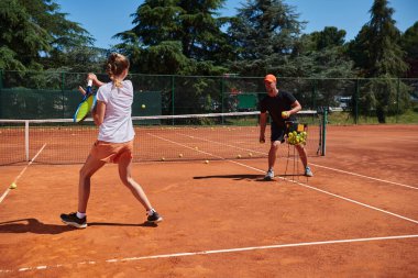 Profesyonel bir tenisçi ve onun koçu tenis kortunda güneşli bir günde antrenman yapıyorlar. Profesyonel bir tenisçinin antrenmanı ve hazırlığı.
