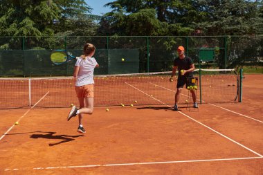 Profesyonel bir tenisçi ve onun koçu tenis kortunda güneşli bir günde antrenman yapıyorlar. Profesyonel bir tenisçinin antrenmanı ve hazırlığı.