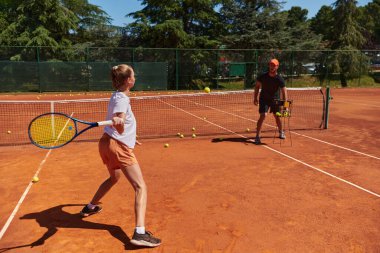 Profesyonel bir tenisçi ve onun koçu tenis kortunda güneşli bir günde antrenman yapıyorlar. Profesyonel bir tenisçinin antrenmanı ve hazırlığı.