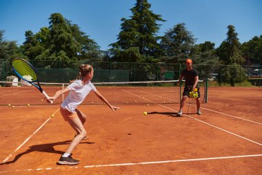 Profesyonel bir tenisçi ve onun koçu tenis kortunda güneşli bir günde antrenman yapıyorlar. Profesyonel bir tenisçinin antrenmanı ve hazırlığı.